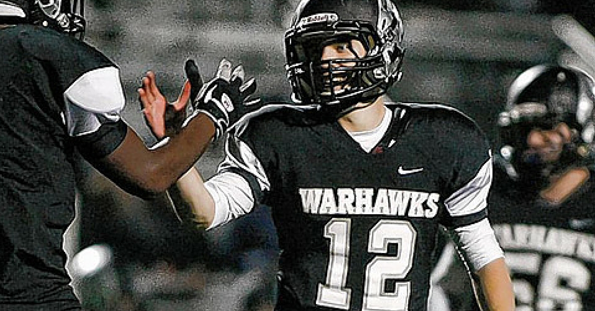 A football player in black uniform with his hands up.