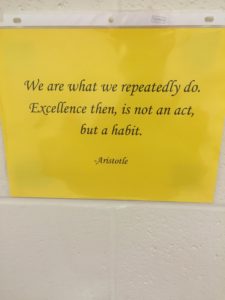 A yellow sign with an aristotle quote on it.