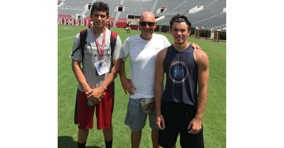 Three men standing on a field with an american football stadium in the background.