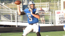 A man in blue and white uniform throwing a football.