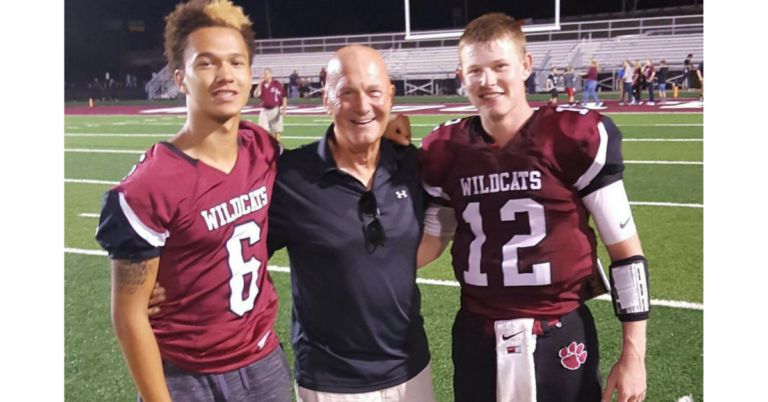 Three men standing on a field with one man wearing a football uniform.