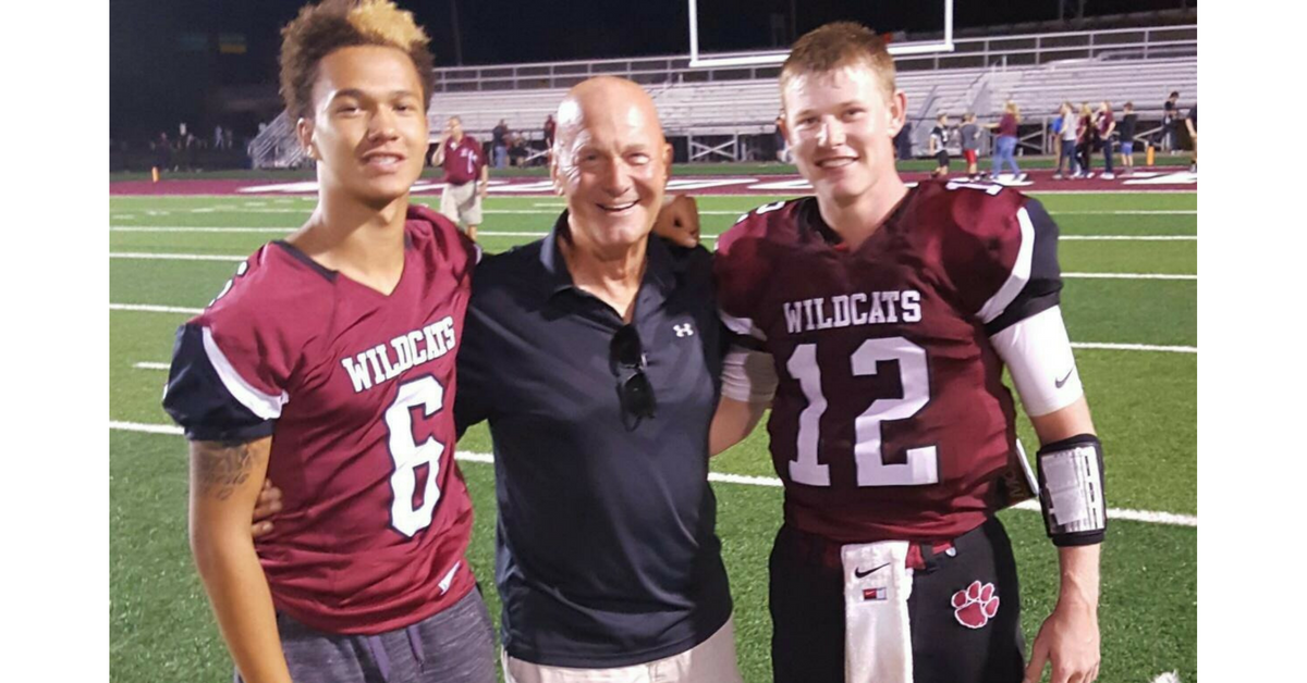 Three men standing on a field with one man wearing a football uniform.