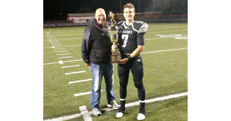 A man and his father holding a trophy on the field