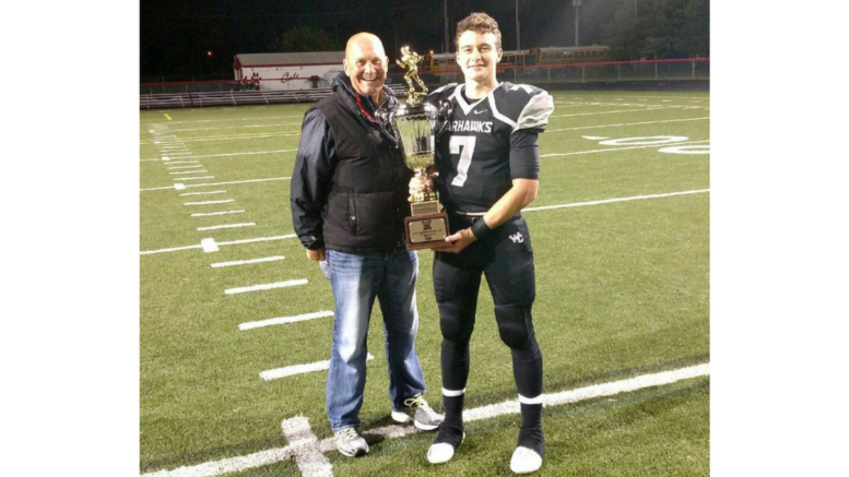 A man and his father holding a trophy on the field