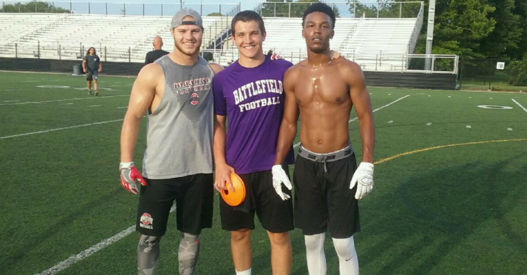 Three men standing on a field with an orange football.