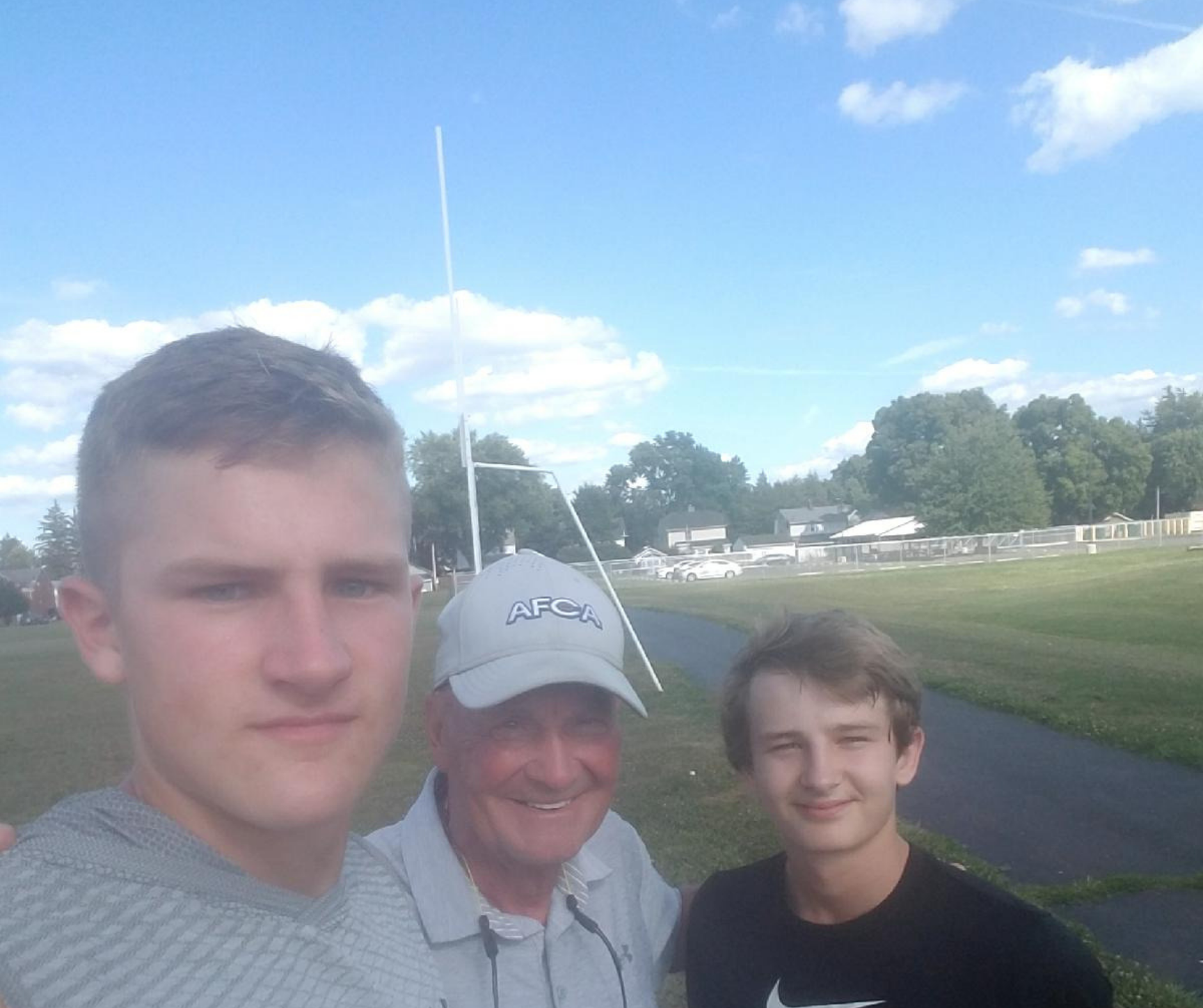 Three men standing in a field with one man holding onto the antenna.