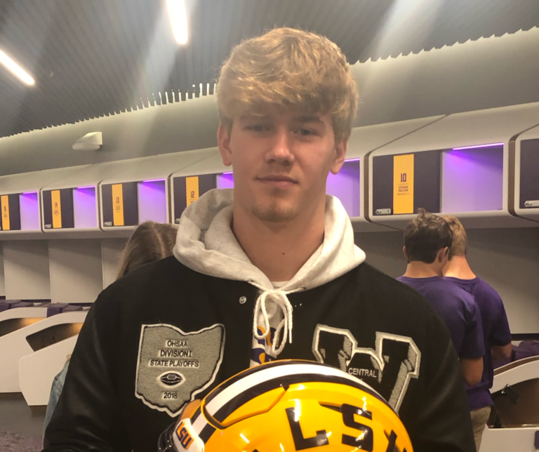 A young man holding a football helmet in a locker room.