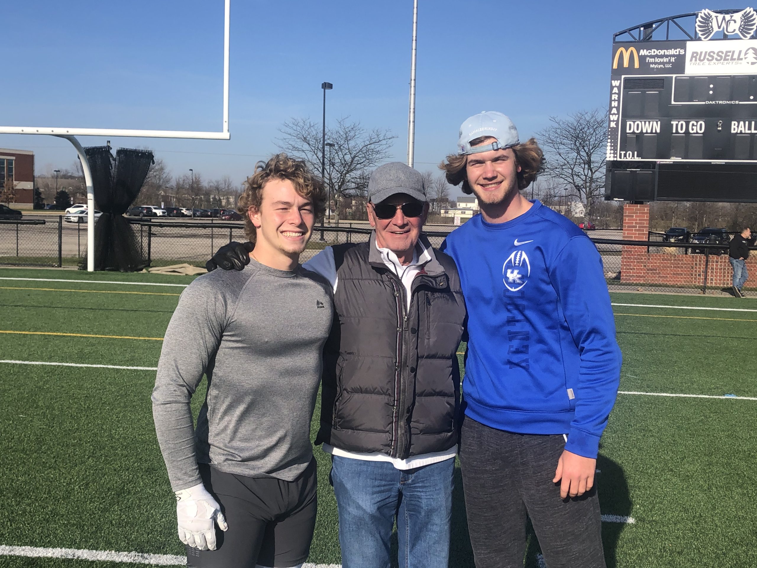 Three men standing on a field with one man wearing glasses.